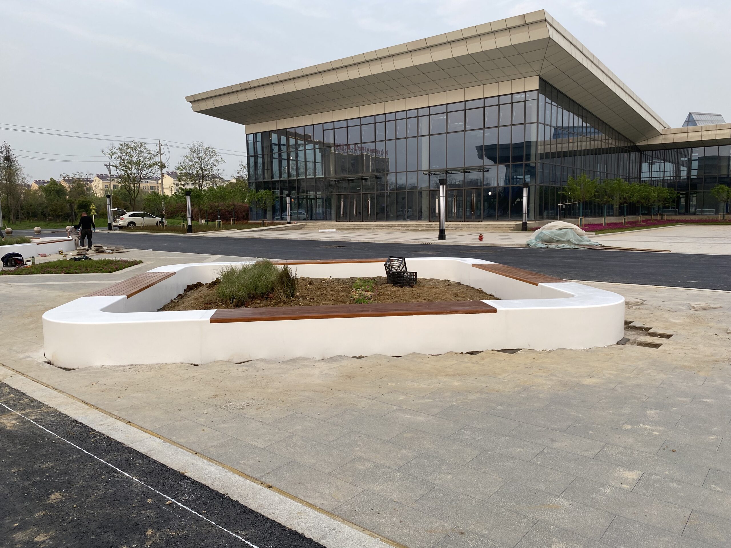 微信图片 20240410153838 scaled 当常州溧阳的现代建筑前需要一处 “造景 + 休憩” 的公共设施,这组阿尔博 UHPC + 防腐木坐凳恰好踩中了空间的质感节奏。 白色 UHPC 主体适配溧阳的温湿气候 —— 耐潮不返碱、暴晒不褪色,长期置于城市公共区域,不用频繁维护也能稳持洁净轮廓;棕调防腐木坐面则贴合江南体感需求,经防腐处理后,梅雨季不易霉变、盛夏坐感不灼人,温润触感中和了硬质材质的冷感。 它既是围合绿植的生态树池,也是可供多人落座的休闲坐具:柔和围合造型自然适配建筑前的开放空间,既为往来人群提供歇脚点,又以 “白 + 棕” 简约配色呼应现代建筑的利落风格,成了溧阳城市配套里的质感细节。 从建筑前的临时休憩,到景观节点的视觉点缀,它把 “实用功能” 与 “地域气候适配” 揉进了溧阳的公共空间里。
